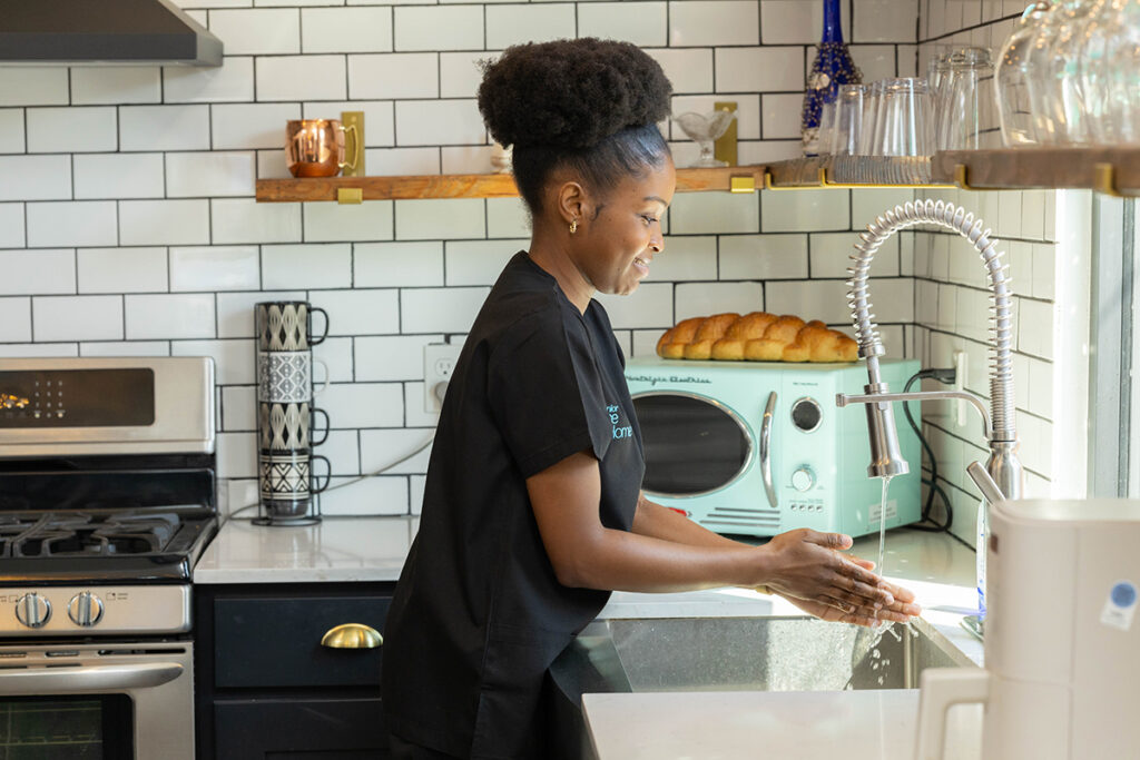 Caregiver washing hands in kitchen during in-home senior care visit