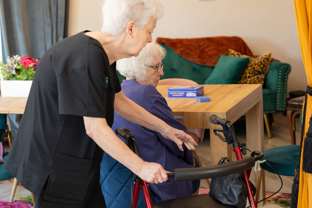 Caregiver assisting senior woman with walker during recovery care at home